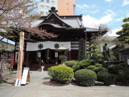 ▲線路を越えると、表参道。中間あたりにかるかや山西光寺。ここにも御開帳のシンボルとも言える回向柱（えこうばしら）が立っている